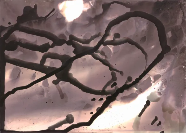 Looping dark drips over a pale, pitted surface