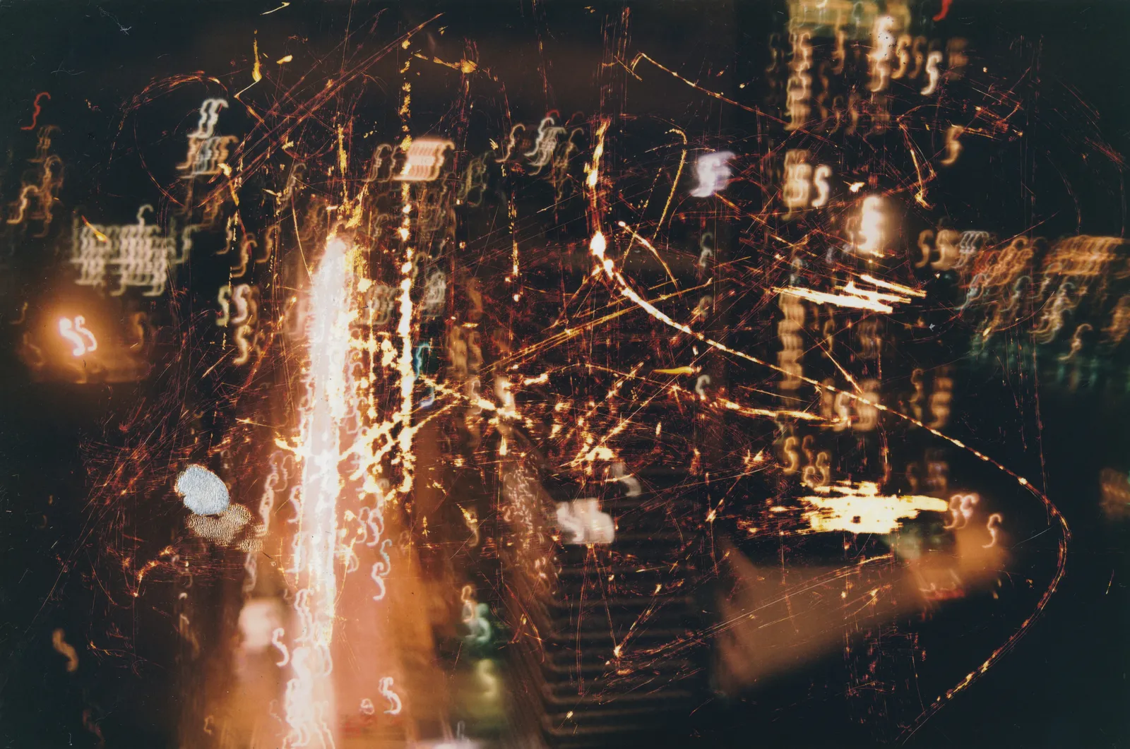 Night photograph of city lights blurred into streaks and squiggles, scratched with fine orange lines